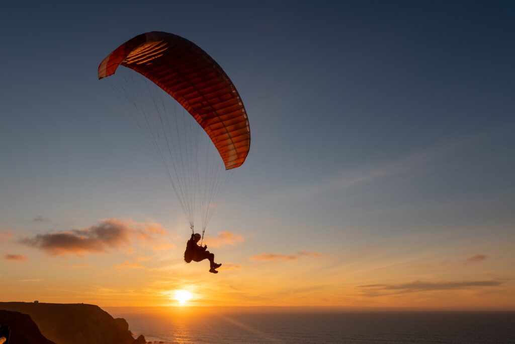 Paraglider flying over thesea shore at sunset. Paragliding sport concept.