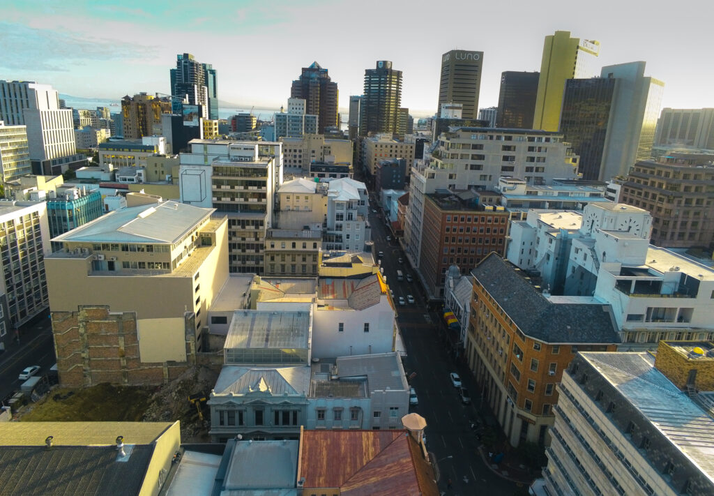 Aerial view of Cape Town city centre with high-rise buildings, historic architecture, and a glimpse of Table Bay in the distance.
