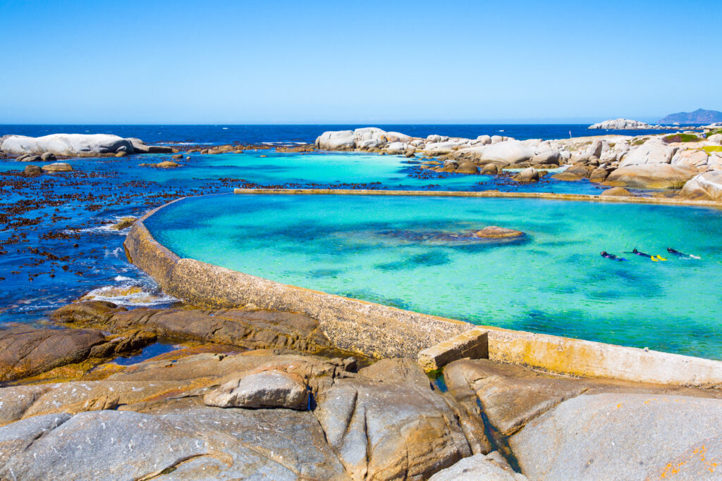 Miller's Point tidal pool near Simon's Town with turquoise water, rocky shoreline, and swimmers enjoying the clear ocean.